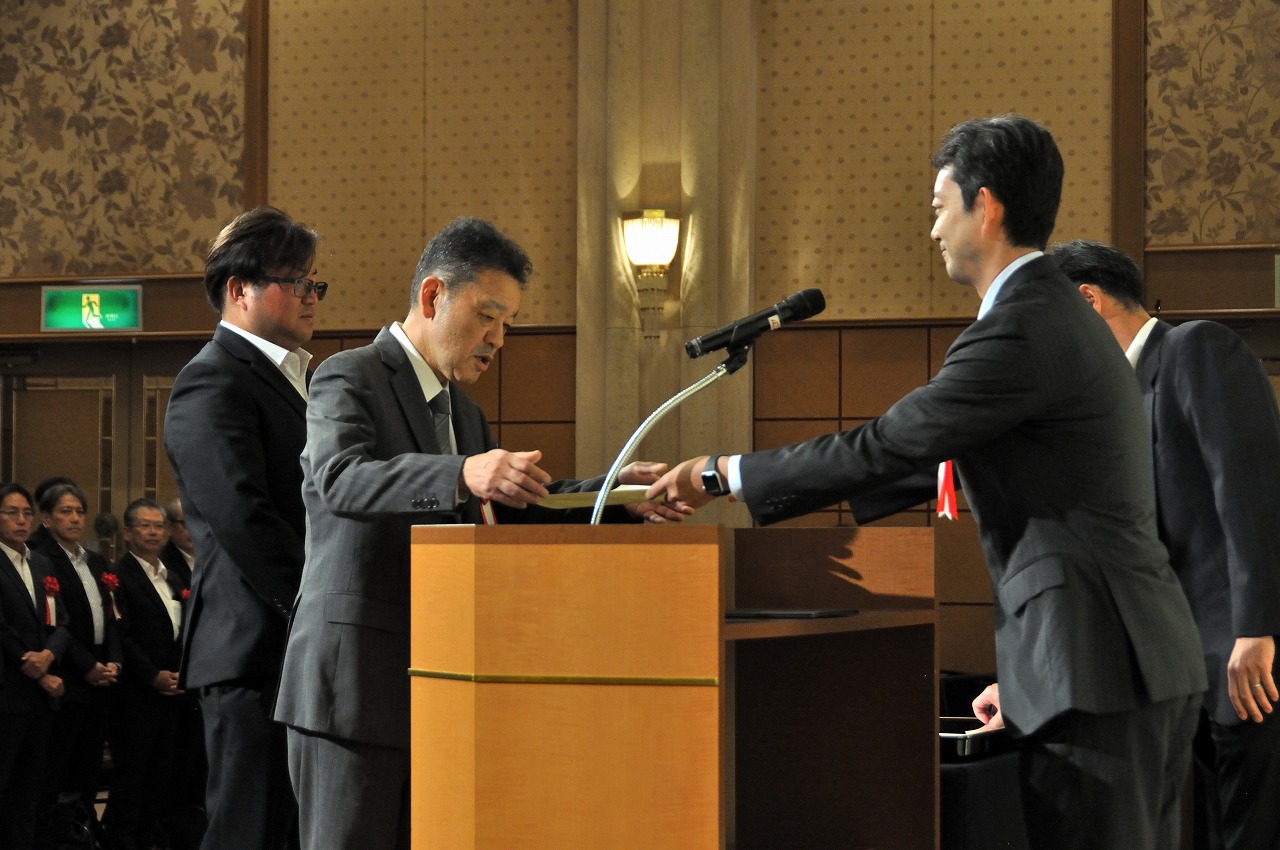 優良建設工事の表彰状を萩原代表取締た役（中央）、優秀技術者の表彰状を小川氏（左）が受け取った